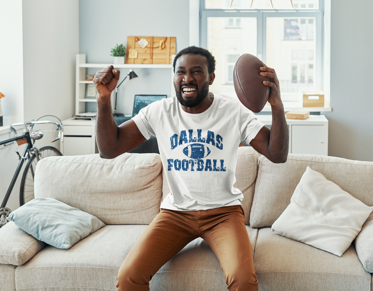Man wearing a white Dallas Football T-shirt while cheering with a football at home