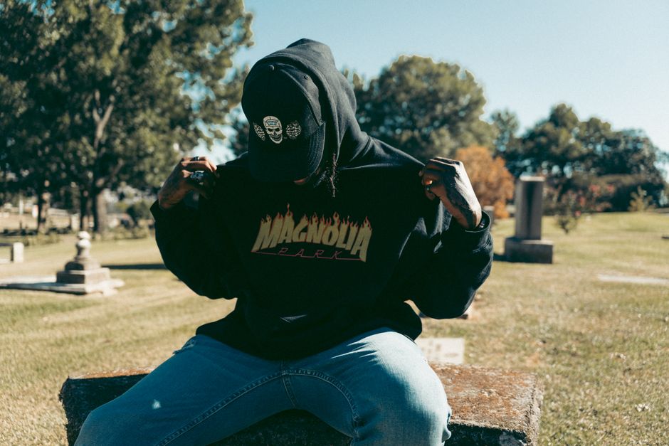 Person in hoodie and cap sitting outdoors, emphasizing casual street fashion.