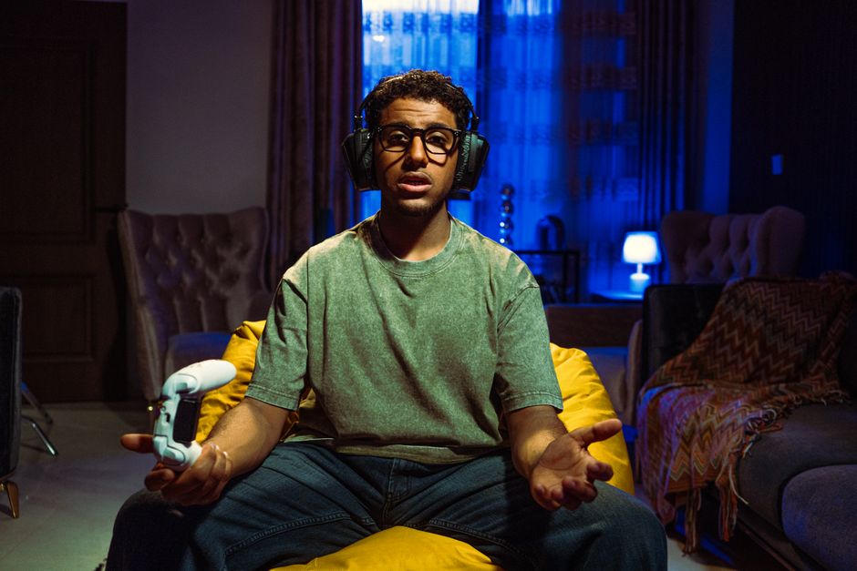 Young man gaming indoors at night, focused on the screen, wearing headphones and holding a controller.