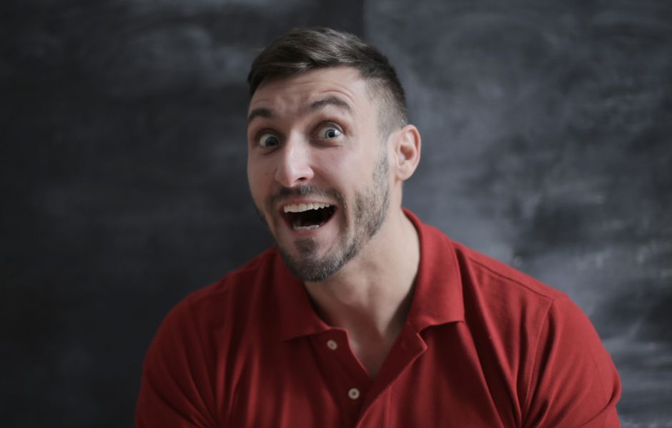 Close-up portrait of a man with a surprised expression wearing a red shirt.