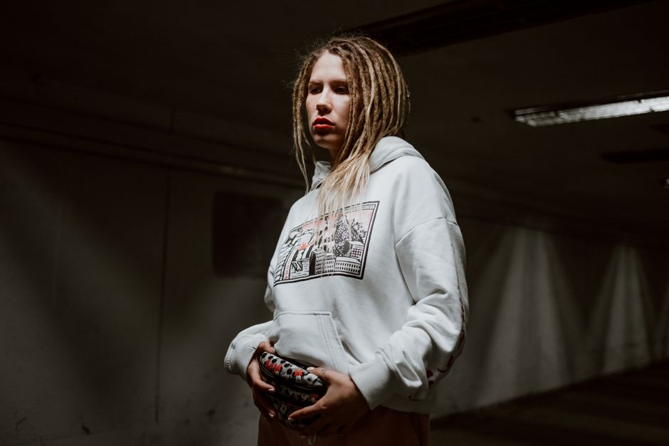 Stylish woman with dreadlocks wearing a white hoodie in a moody urban setting.