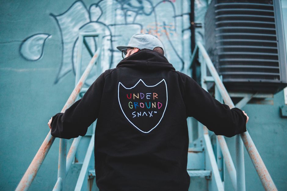 Back view of hipster man in black hoodie and cap standing on metal stairs and looking away