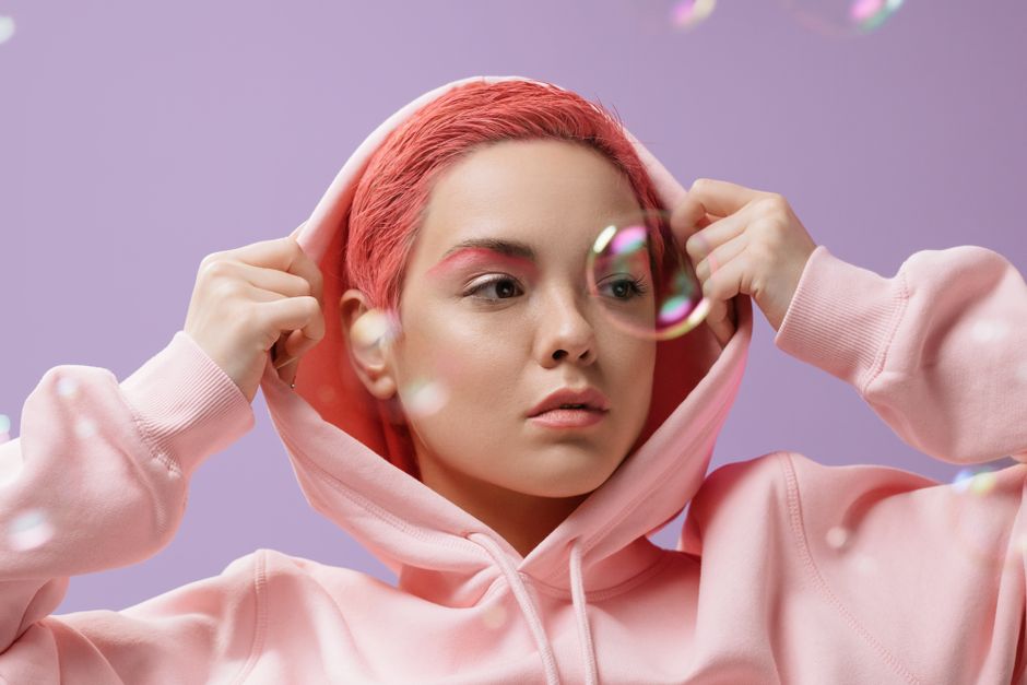 Young woman posing in pastel pink hoodie with bubbles on a violet background.