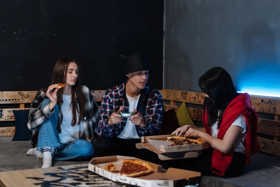 Group of friends sharing pizza while playing video games, enjoying leisure time indoors.