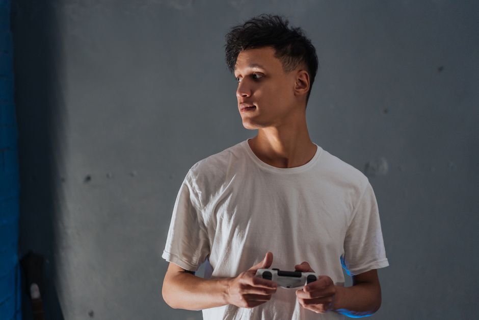 A young man wearing a white t-shirt focuses intently while holding a game controller indoors.