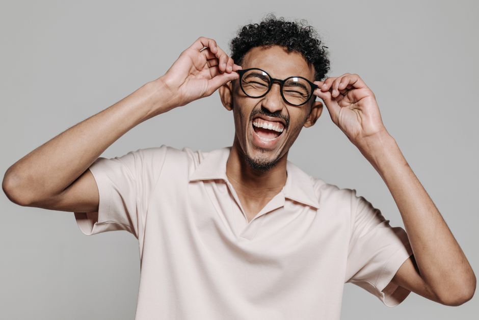 A cheerful man with eyeglasses laughs energetically in a studio environment.