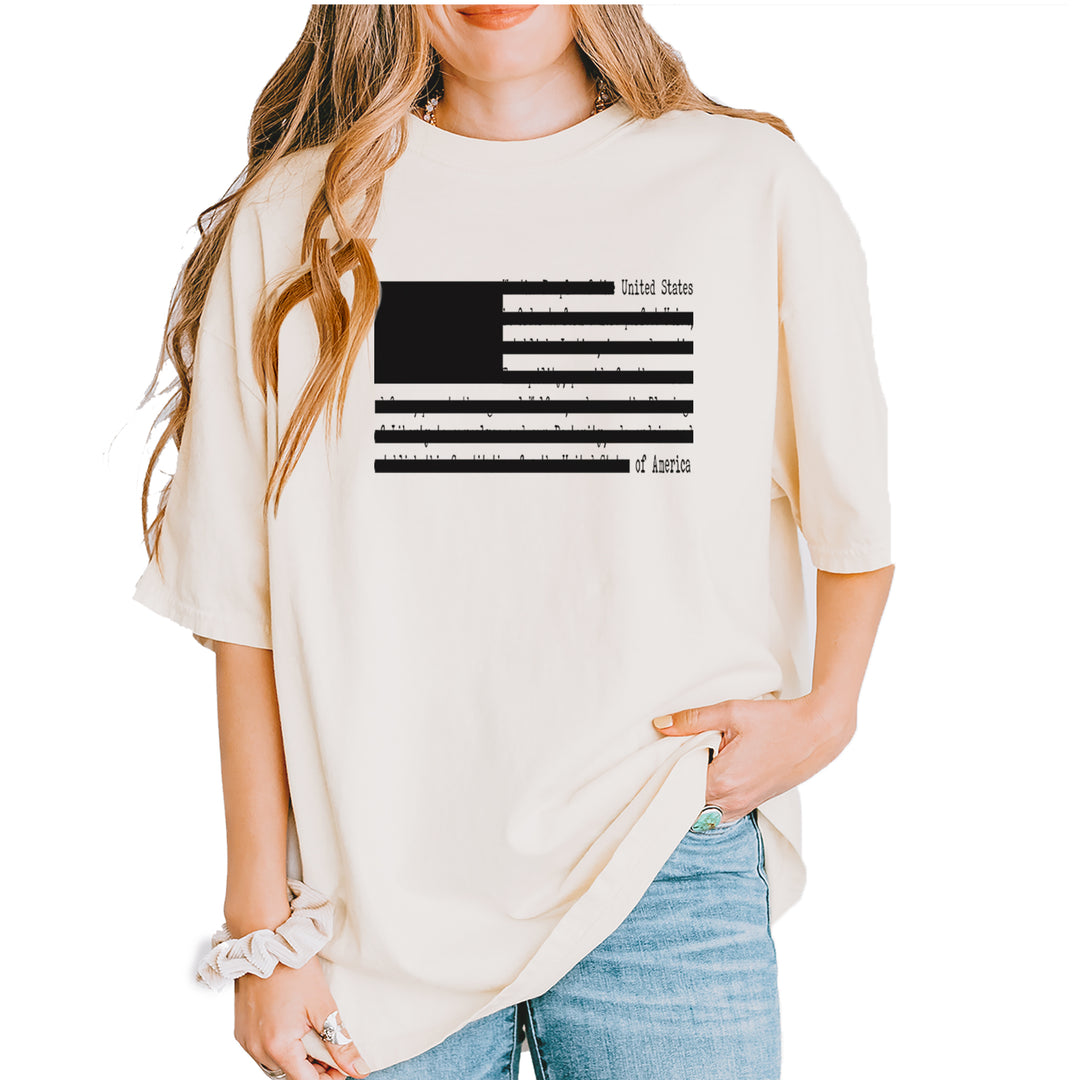 Black-and-white American flag with redaction-bar stripes over faint document text on a Comfort Colors 1717 unisex T-shirt